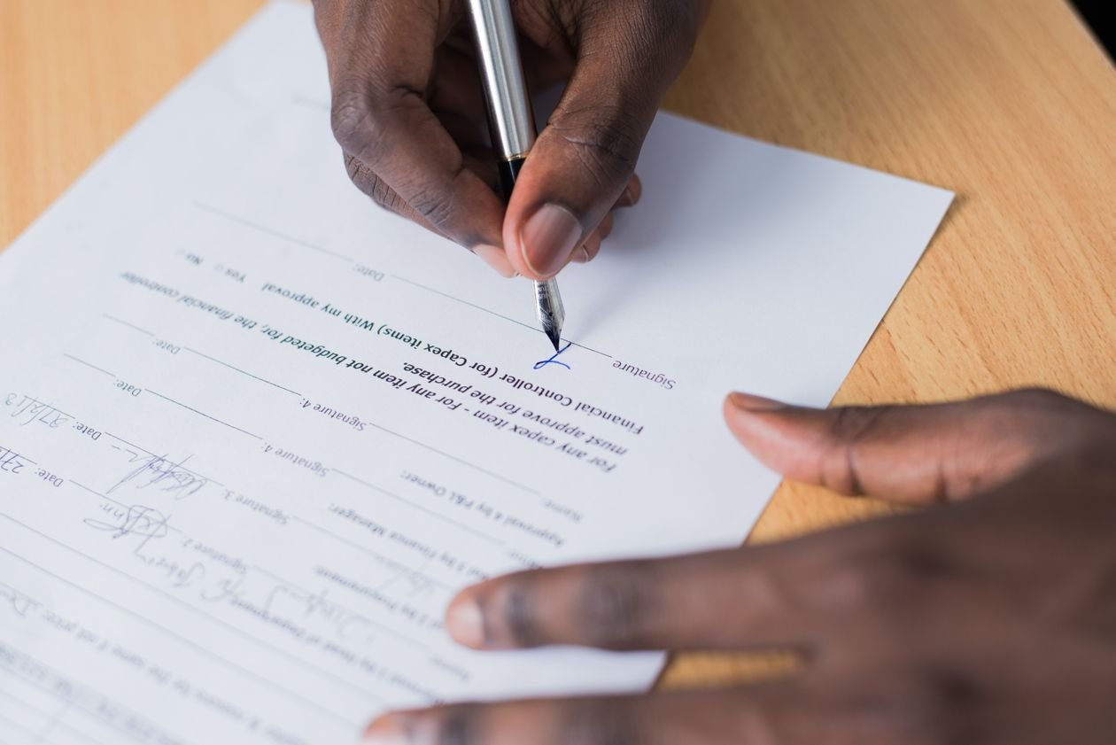 Hand signing a contract with a pen on a desk