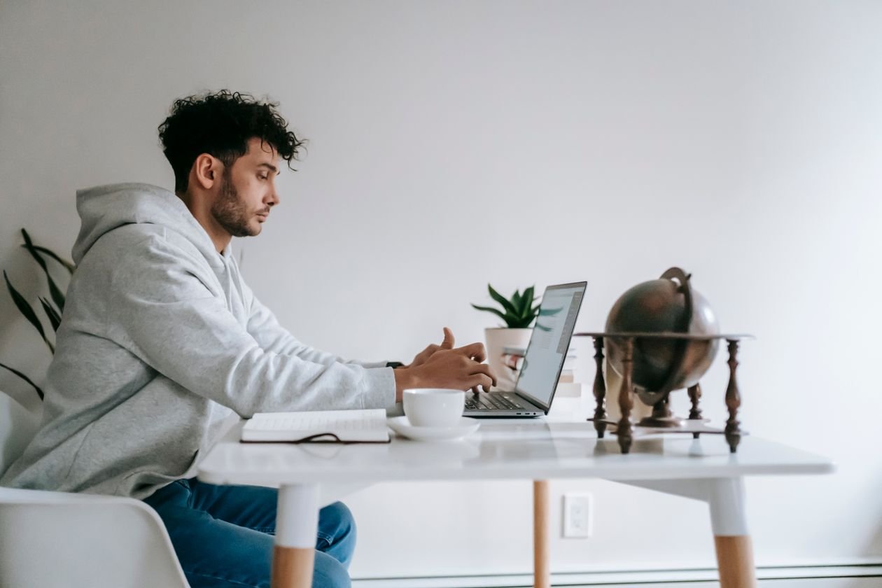 Man working on a laptop at a home office table with coffee